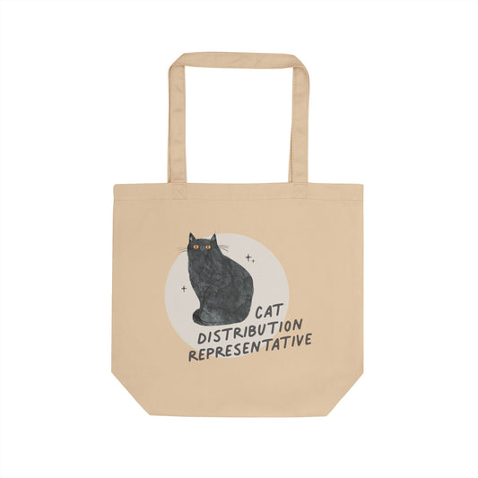 A beige canvas tote bag with two handles, featuring a graphic of a black cat sitting in front of a white circle with the text 'CAT DISTRIBUTION REPRESENTATIVE'.