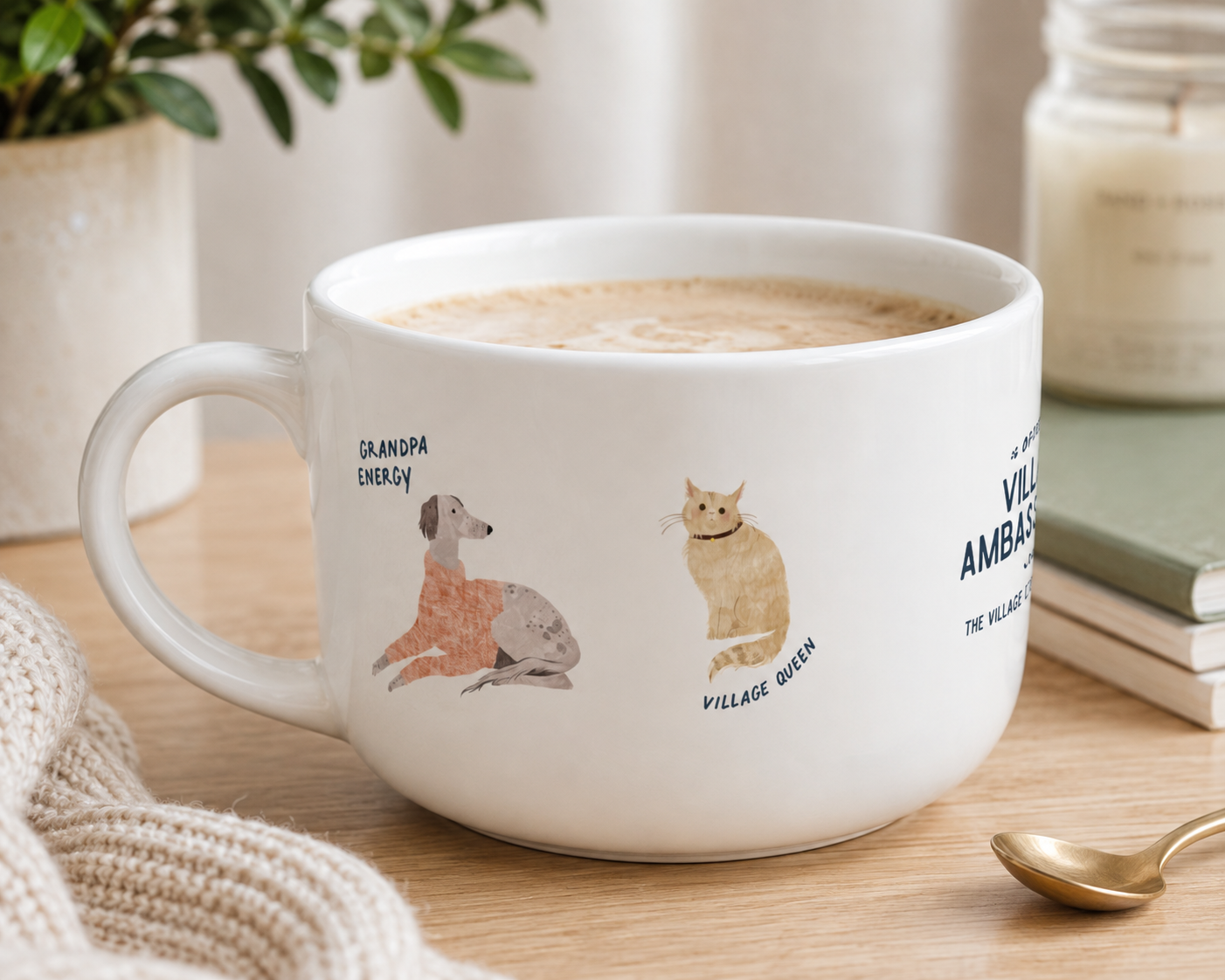 A white ceramic coffee mug filled with a latte sits on a wooden table in a cozy setting. The mug features illustrations of a dachshund labeled 'DAMBOA ENERGY' and a tabby cat labeled 'VILLAGE QUEEN'.